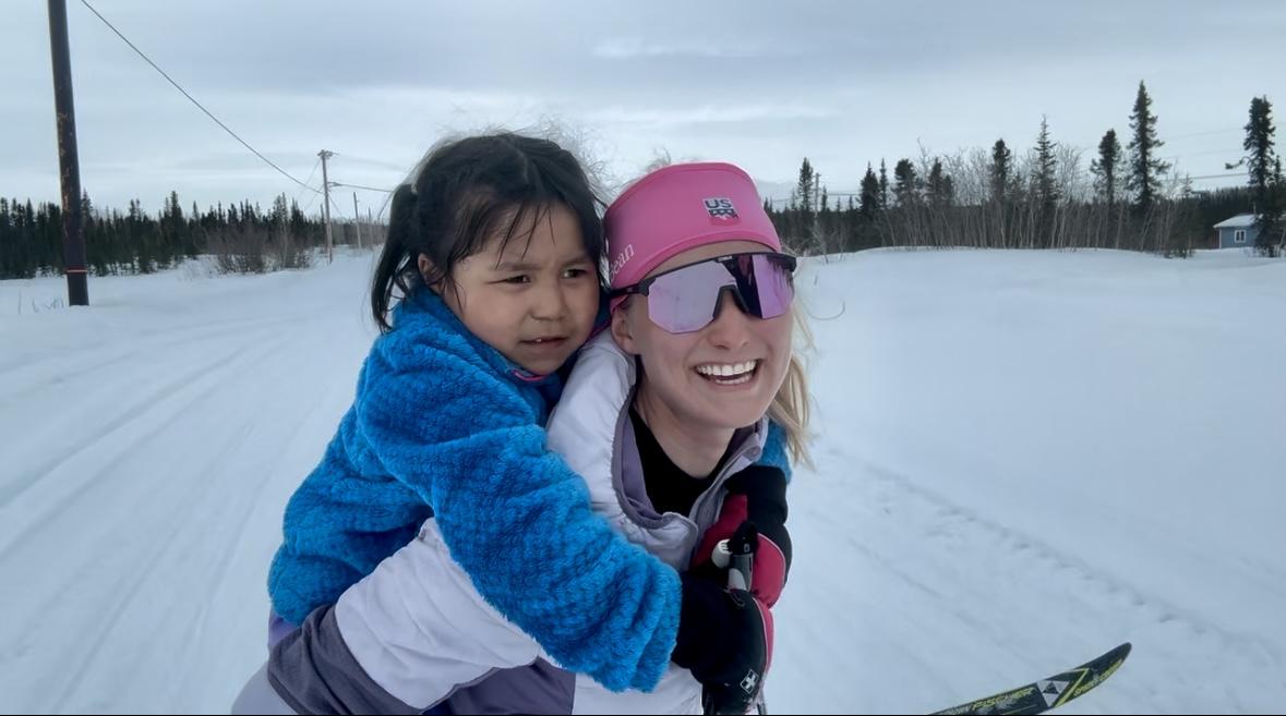 A person carrying a child on her back in the snow
Description automatically generated